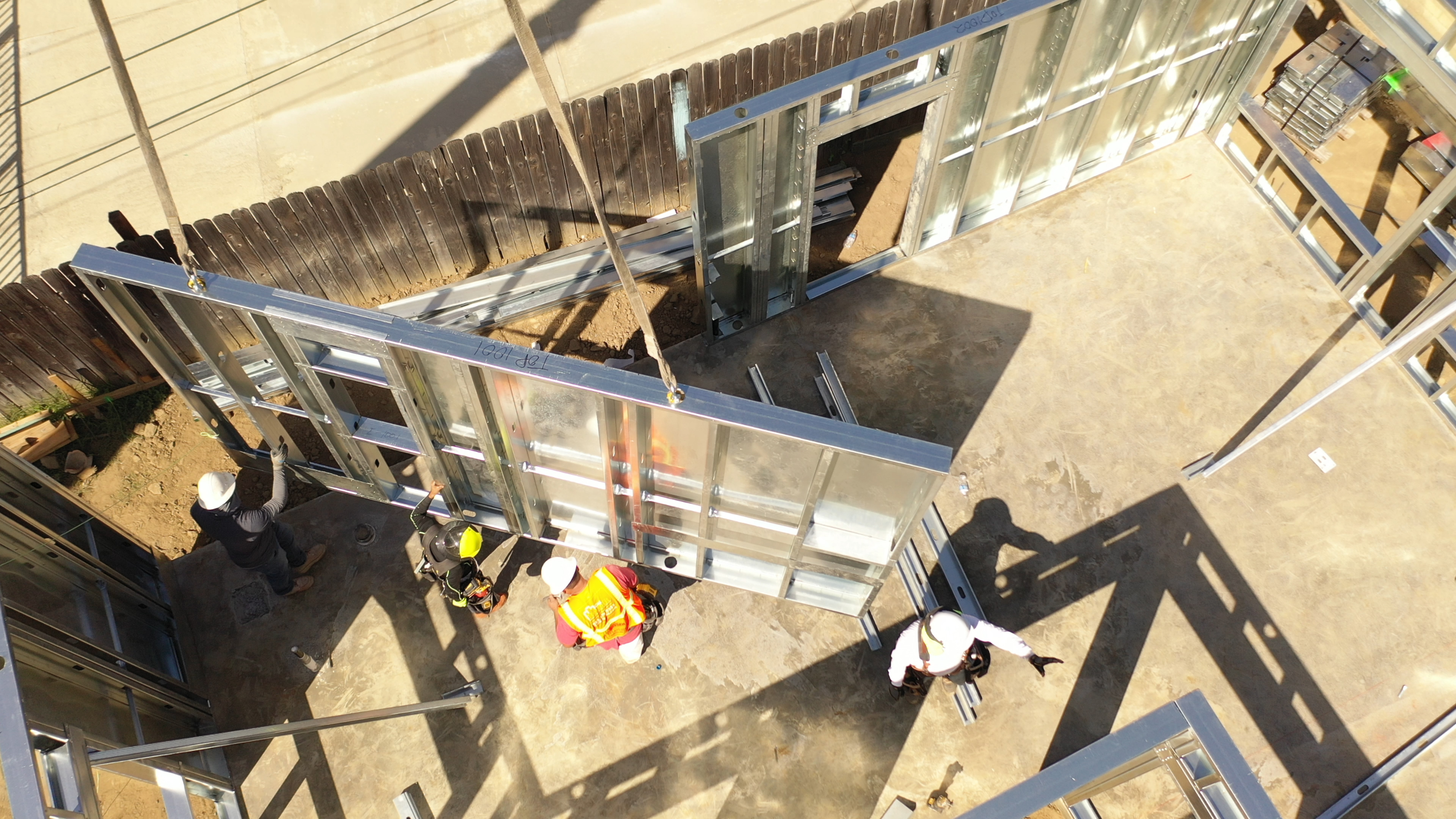 Aerial view of a crew craning a panelized light gauge steel wall panel into place on a ground-up jobsite