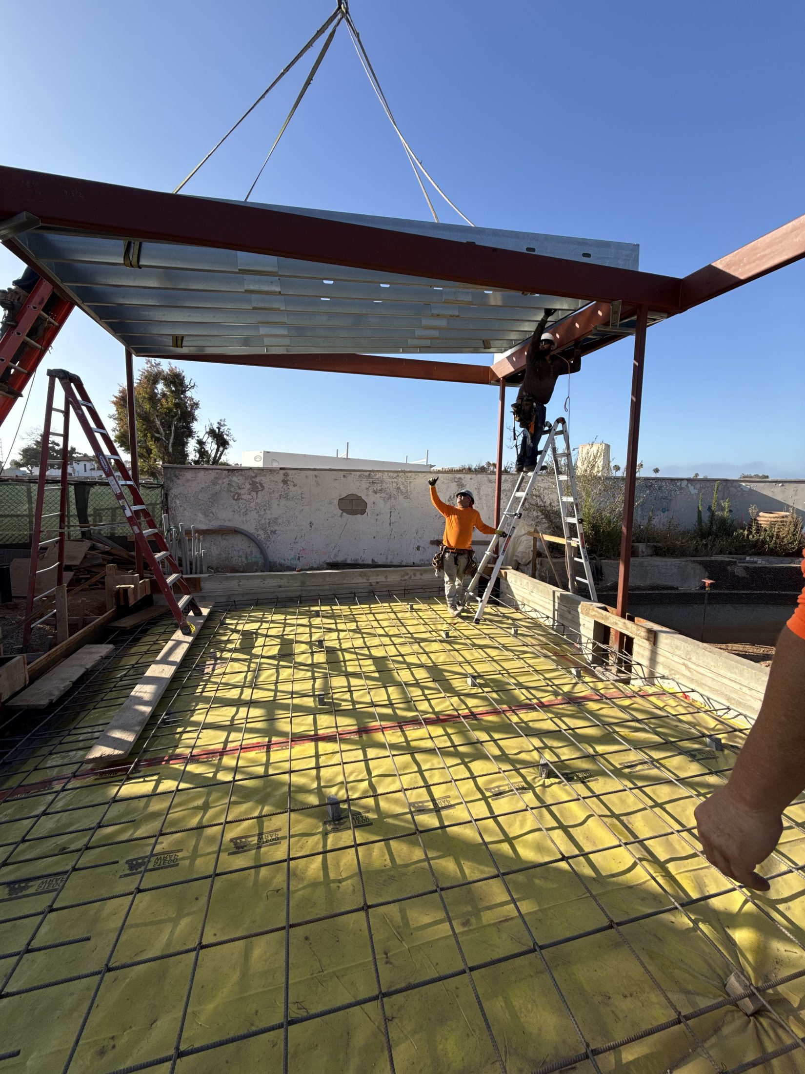 A crane lifts a structural steel beam into place overhead at 777 Ocampo