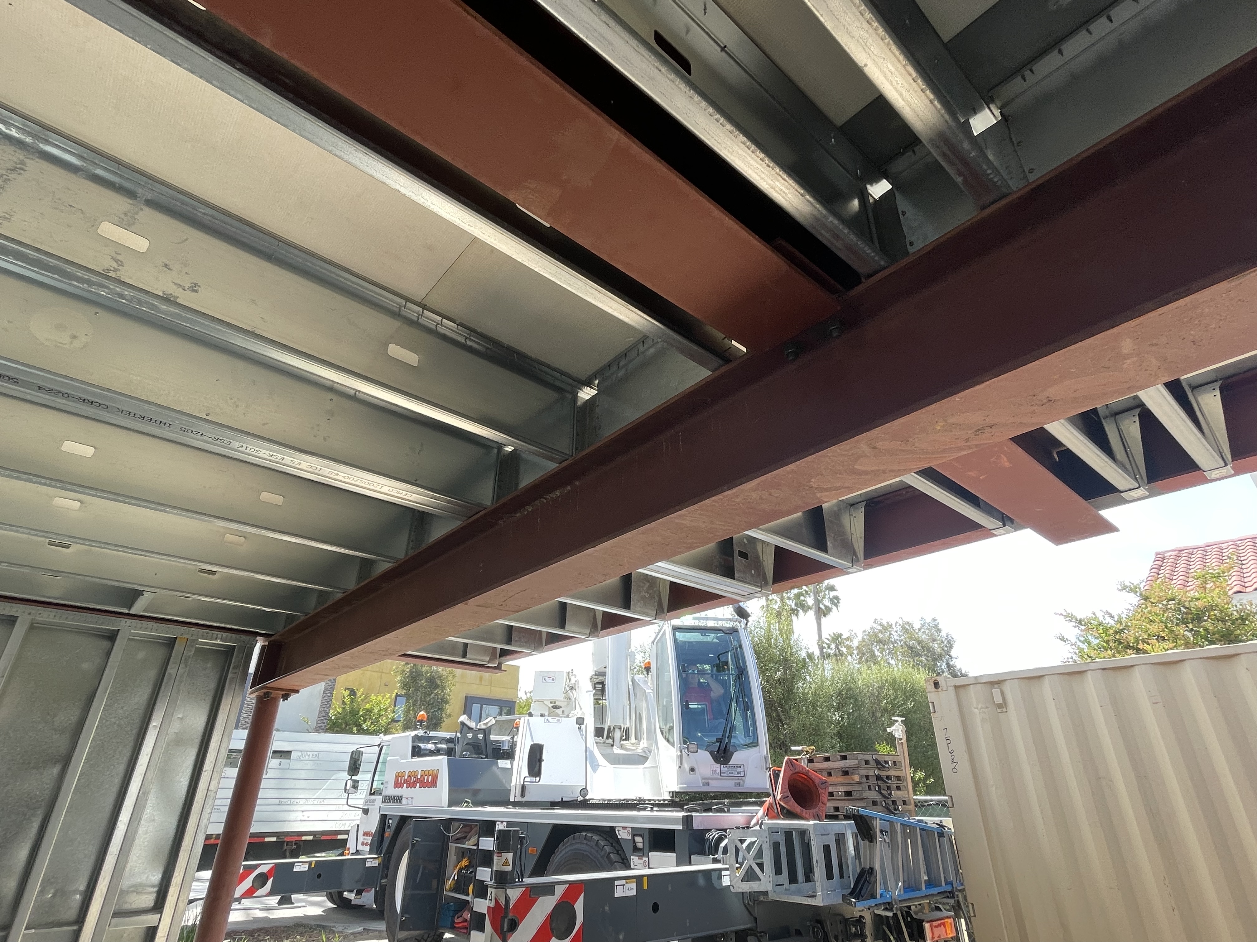 Structural steel beams and light gauge steel floor framing set on site, with a mobile crane working below